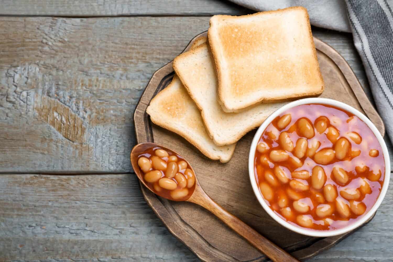 Toasts and delicious canned beans on wooden table, top view. Space for text