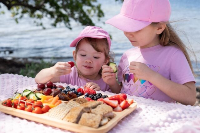 Two kids eating healthy snacks from the charcuterie board outdoors. Kids on the picnic. Healthy eating and kids concept