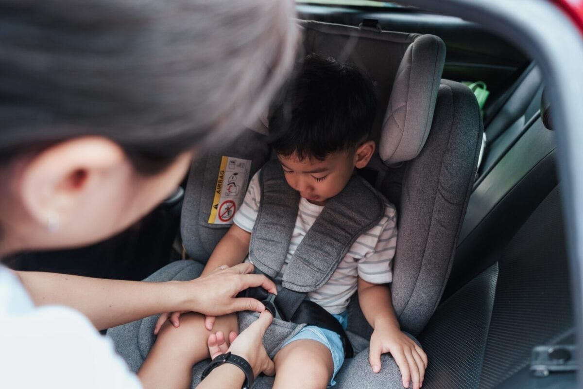 Mom strapping child safely into car seat before departure. Real-life family travel preparation scene highlighting child safety, parental care, and on-the-go lifestyle.