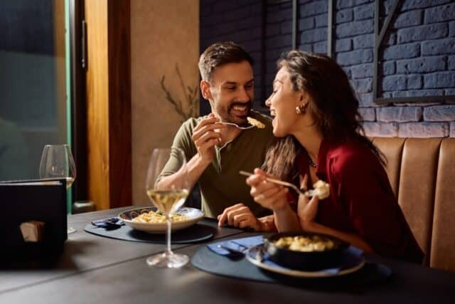 Young happy man sharing his food with a girlfriend while eating in a restaurant.
