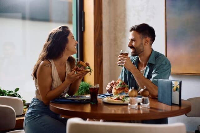 Young happy couple eating pizza and talking in a restaurant.