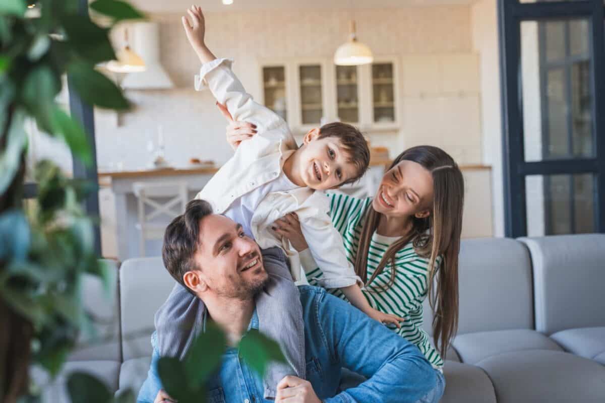 Happy young Caucasian family play together on couch at home. Young mother father and child son boy enjoying happy relax spending time together in modern living room. Care and love concept