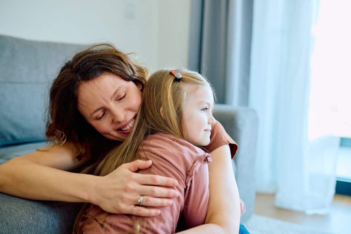 Warm moment of a smiling mother hugging her young daughter at home, showing affection, comfort, and family bonding