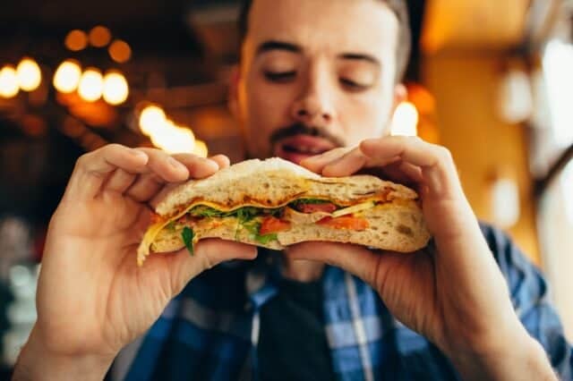 Handsome man sitting in a restaurant and looking at hamburger. He is going to taste that big delicious dish. Young guy having his lunch