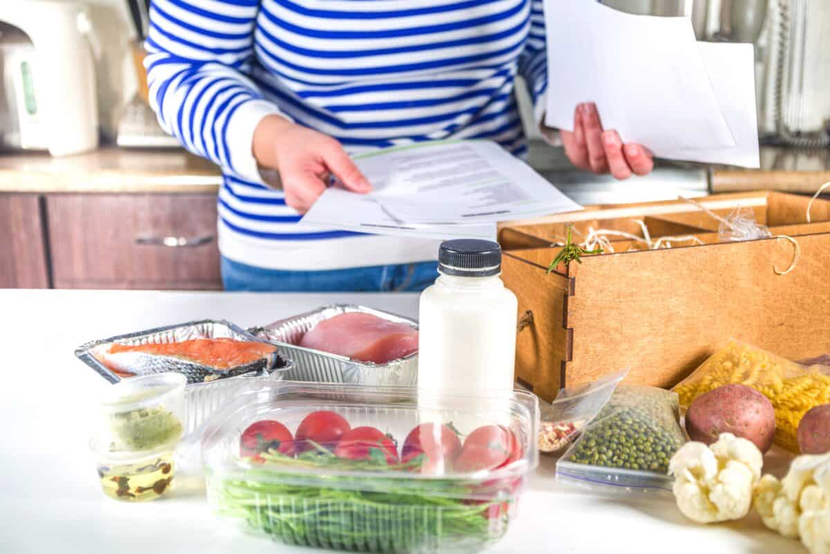 Caucasian woman take apart box with delivery of ingredients, recipes. Meal Kit Delivery Concept. Set various healthy foods with recipes for cooking. Online ordering of restaurant chef grocery delivery