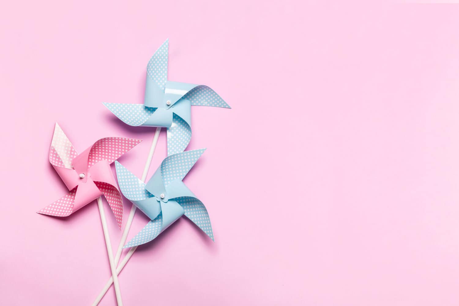 Pink blue paper spinners on light pink background. Kids toys colorful pinwheels on celebration party background. Top view, flat lay.