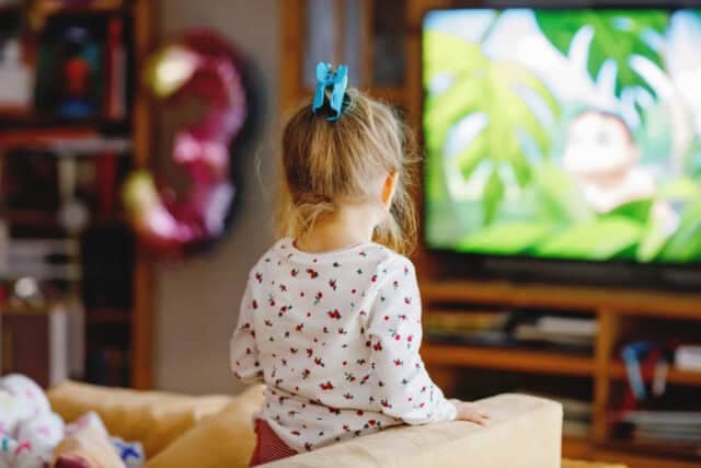 Cute little toddler girl in nightwear pajamas watching cartoons or movie on tv. Happy healthy baby child at home