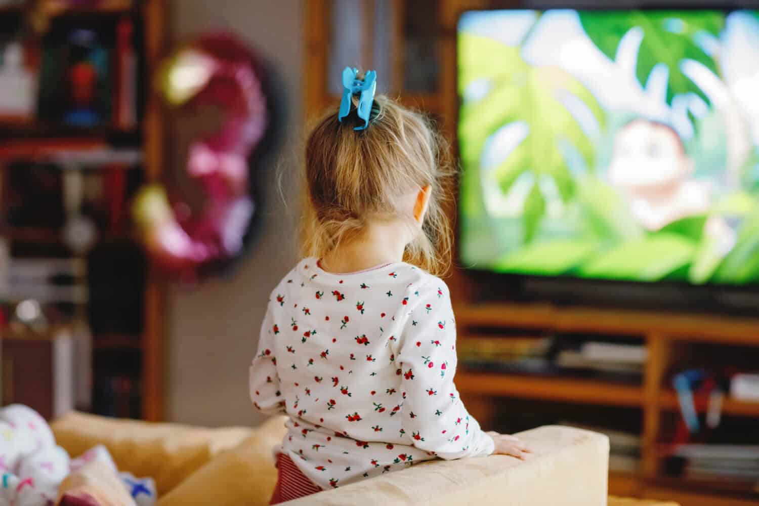 Cute little toddler girl in nightwear pajamas watching cartoons or movie on tv. Happy healthy baby child at home