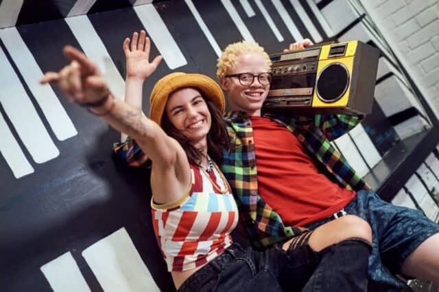 Portrait playful, cool young friends gesturing, listening to music with ghetto blaster at painted wall