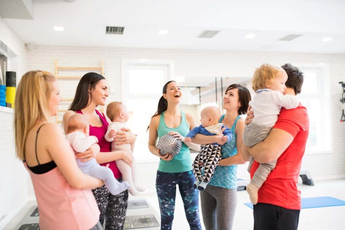 Group exercise class, mother working out with baby in gym. Moms staying active while boding with babies. New parent friends.