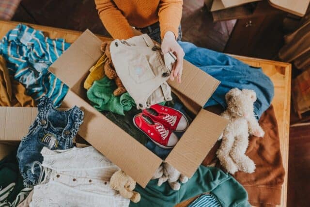 Close-up of woman sorting an old out-of-use kid toy, clothes and shoes in box for charity or converting discarded materials. Upcycling concept.