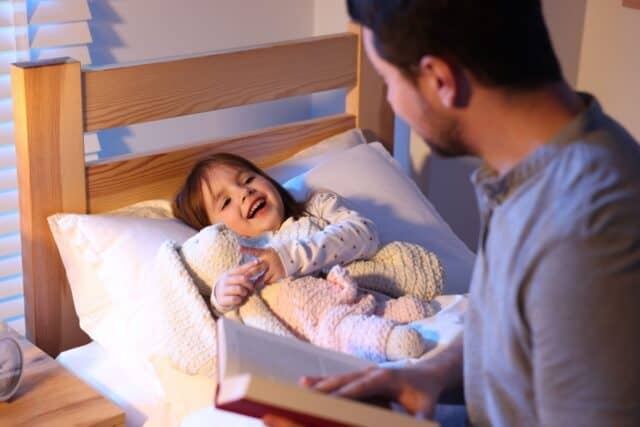 Father reading bedtime story to his happy daughter at home, selective focus