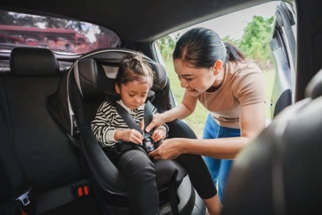 mother is fastening safety belt to toddler girl in a car seat, safety baby chair travelling