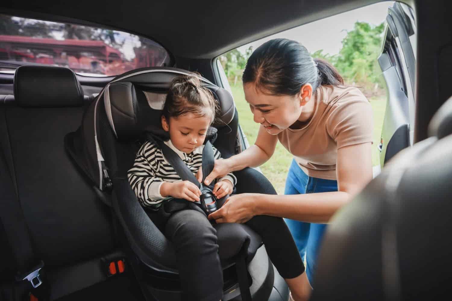 mother is fastening safety belt to toddler girl in a car seat, safety baby chair travelling