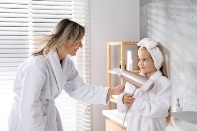 Little girl blow drying her mom's hair in bathroom