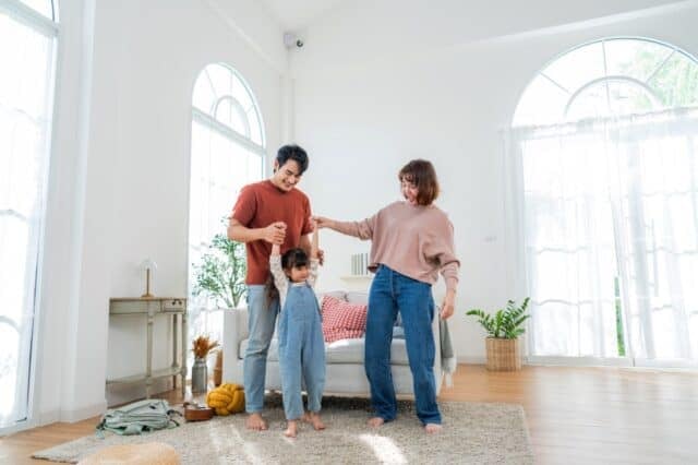 A family is spending time together in their living room. They are playing and laughing with their child, creating happy moments on a weekend morning at home.