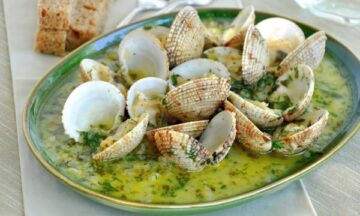 An image of clams/cockles cooked in white wine, with garlic, herbs and olive oil served on a green plate.