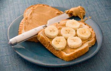 A peanut butter and banana sandwich on a blue plate and placemat. Ready to be consumed.