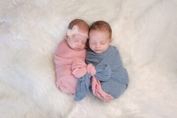 Two month old, boy and girl fraternal twin babies. They are sleeping and swaddled together in pink and blue wraps that are tied together in a bow.