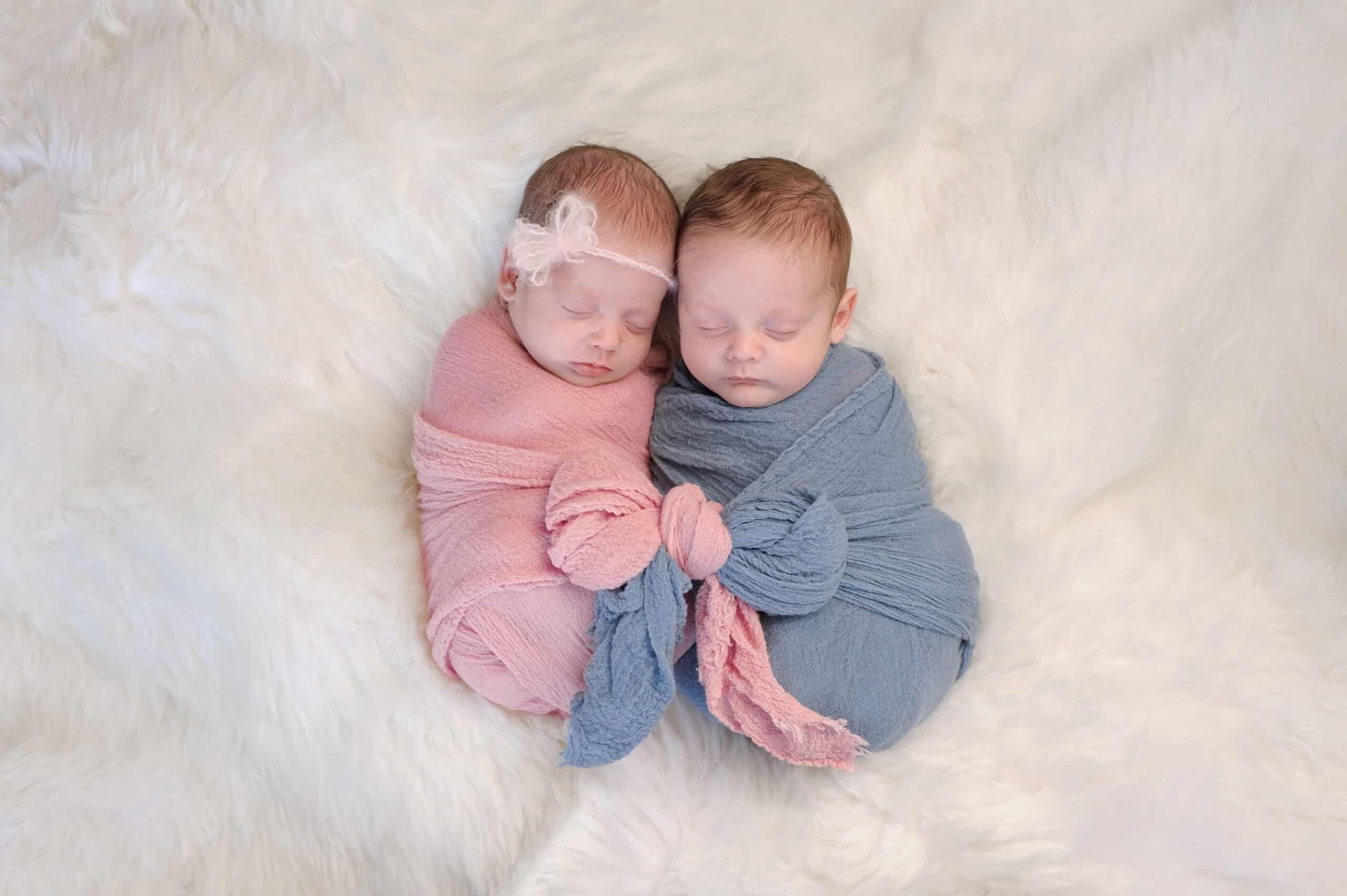 Two month old, boy and girl fraternal twin babies. They are sleeping and swaddled together in pink and blue wraps that are tied together in a bow.