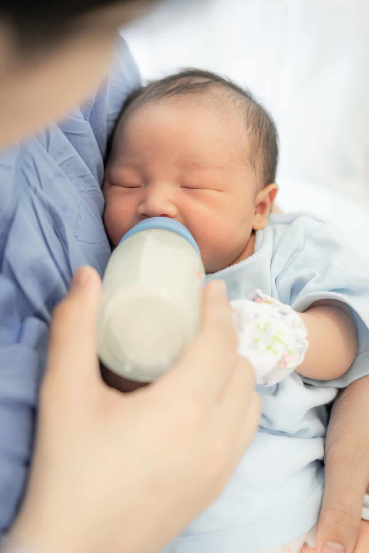 A newborn baby little boy who sleeps the first days of life in a hospital drinking milk from a bottle in the mom's arms.