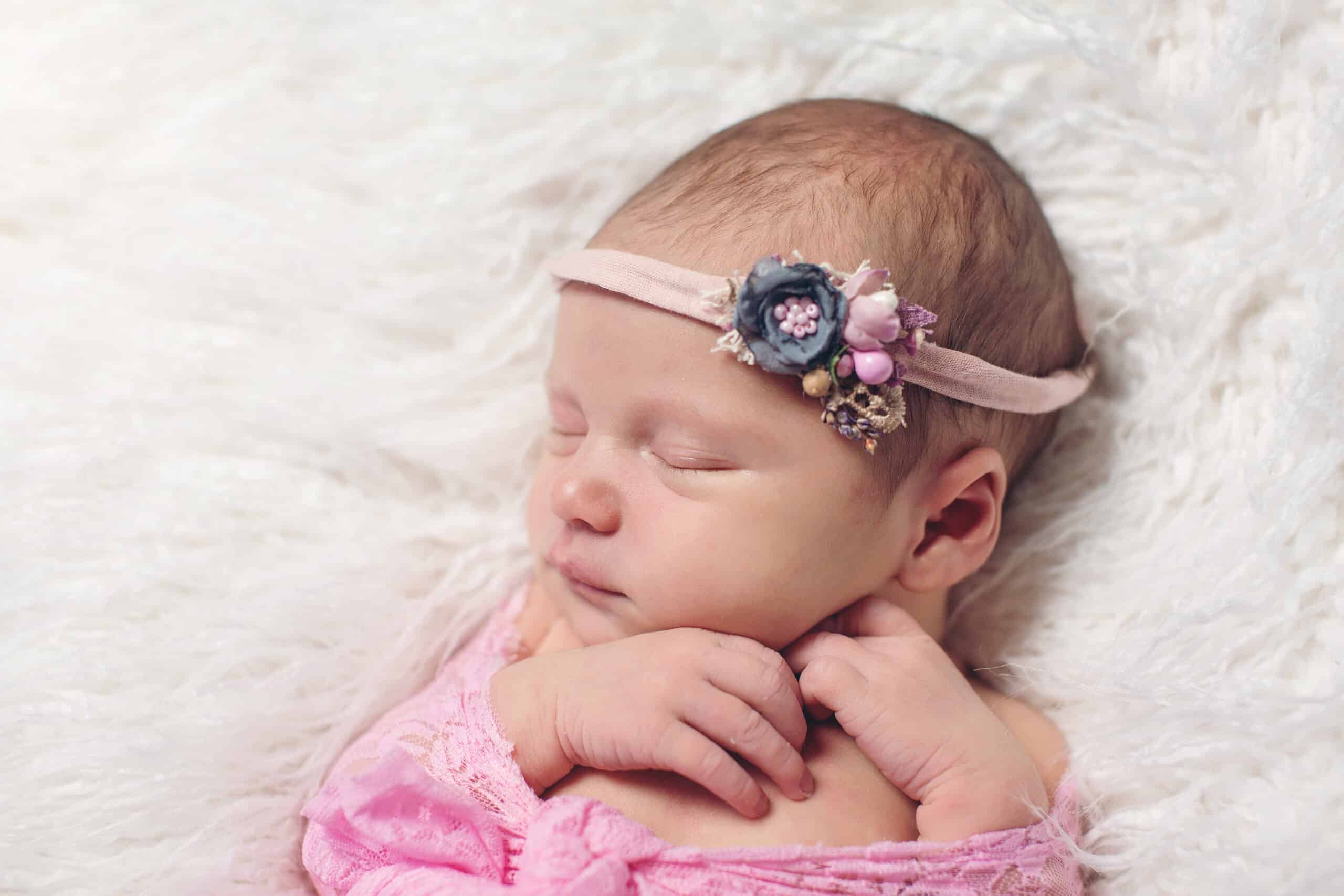 small newborn cute baby, infant girl sleeping in a basket in a flowered dressing on a rug in a hat with a toy, tenderness love care, angel smile, pink-blue color in a flower dressing bunny