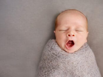 yawning baby swaddled with eyes closed