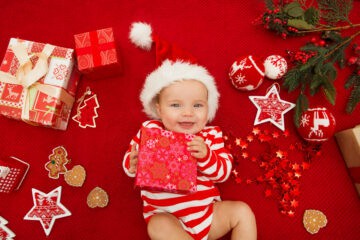 Baby in a striped onesie with Santa hat holding present