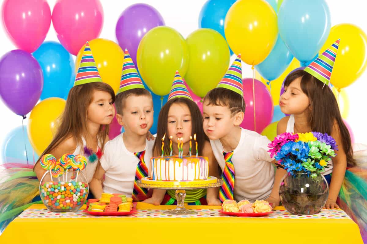 Group of joyful little kids celebrating a birthday party and blowing candles on the cake. Holidays concept.