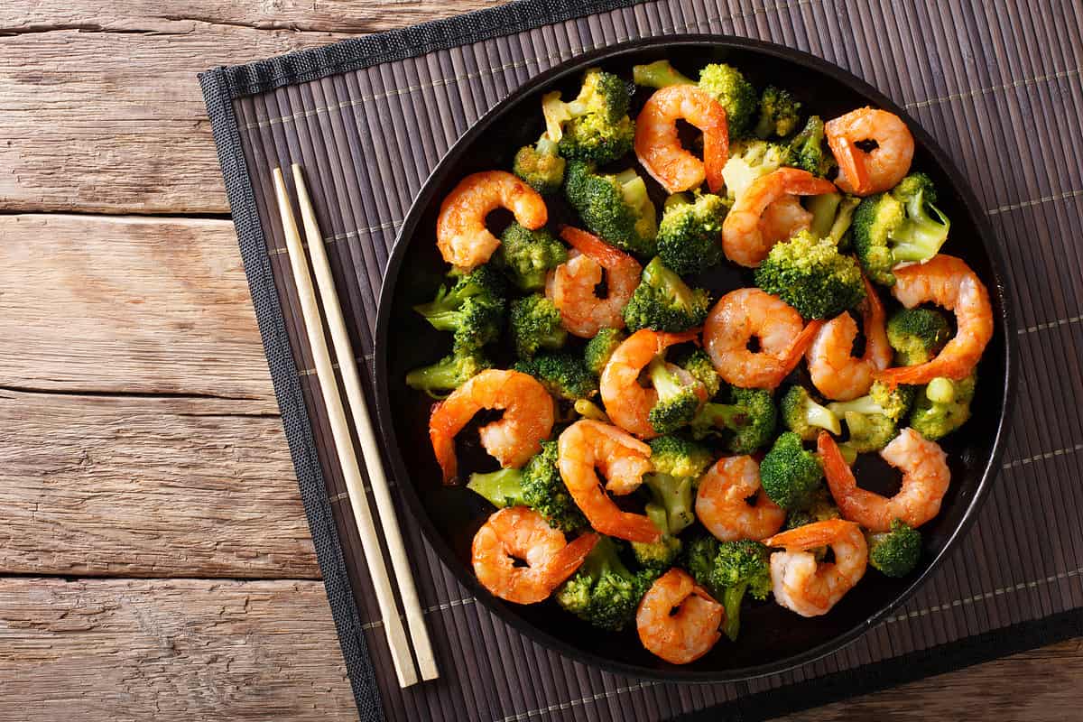Stir frying shrimp with broccoli closeup on a plate. Horizontal top view from above