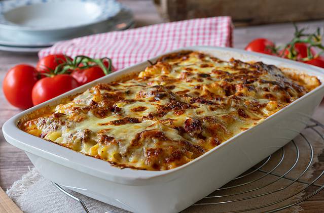 Delicious homemade Italian gratin dish with home-cooked bolognese sauce and bechamel sauce topped with mozzarella cheese and served in a white baking dish on rustic table background. Closeup view