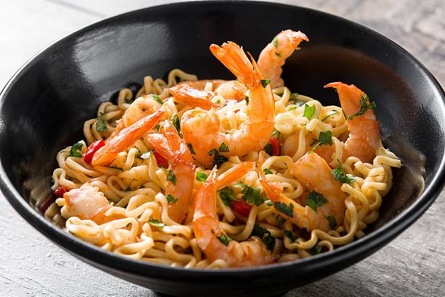 Noodles and shrimp with vegetables in black bowl on slate background