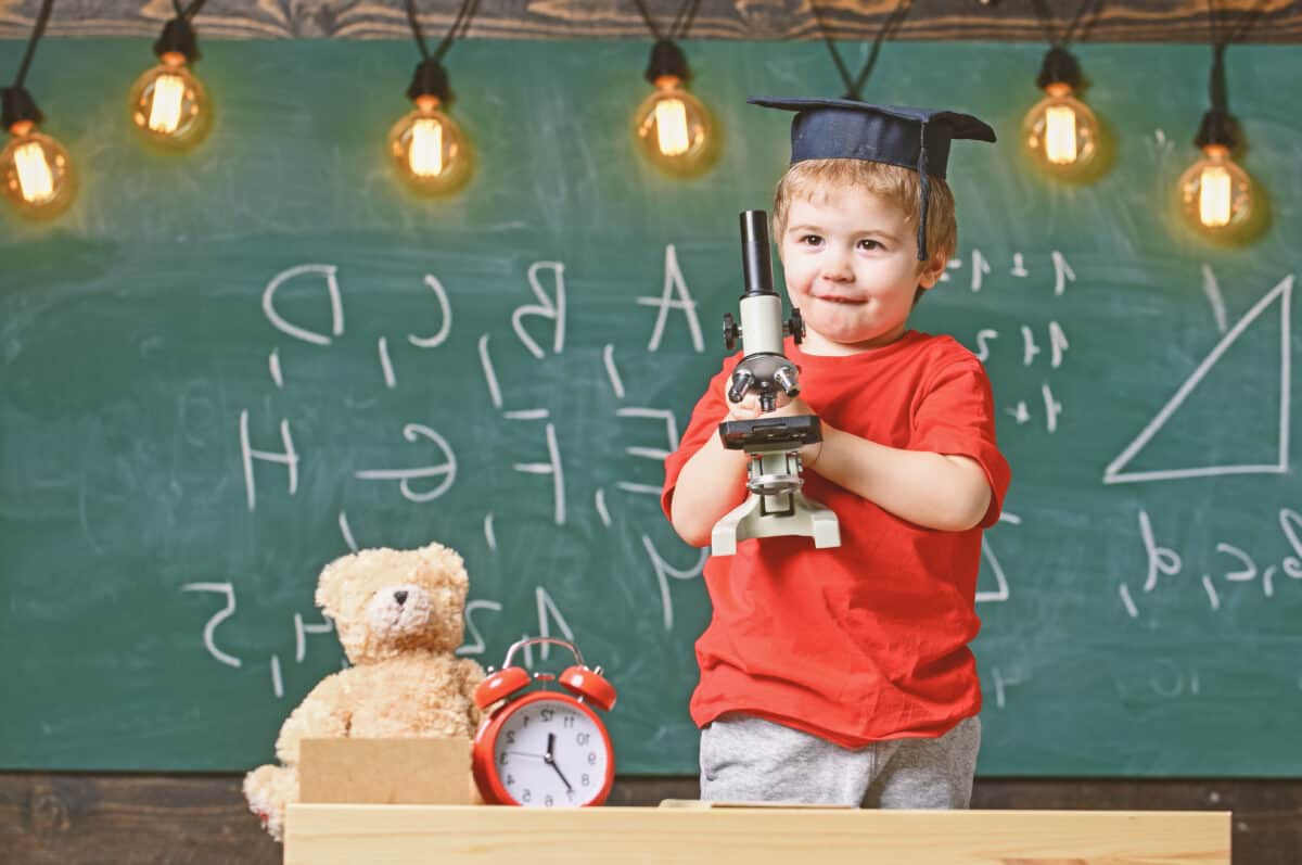 A young student in class holding a microscope enthusiastically.