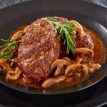 a portion of delicious hot savory juicy Salisbury beef steaks with mushroom onion gravy served on black plates on a wooden table, view from above