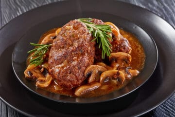 a portion of delicious hot savory juicy Salisbury beef steaks with mushroom onion gravy served on black plates on a wooden table, view from above