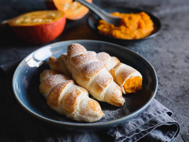 Pumpkin Crescent Rolls are easy to make and bake - Baked crescent rolls with pumpkin filling on plate next to a sliced pumpkin and bowl of pumpkin filling