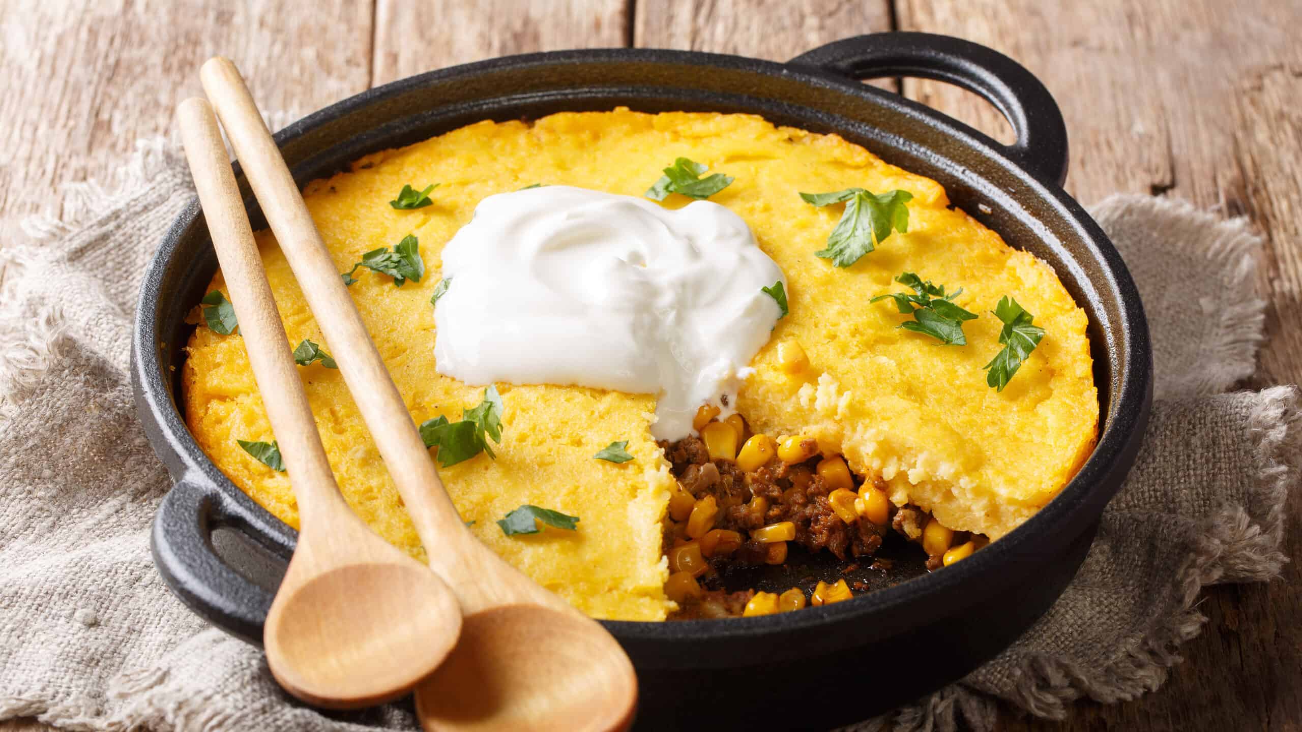 Tamale pie casserole served with sour cream close-up in a pan on the table.