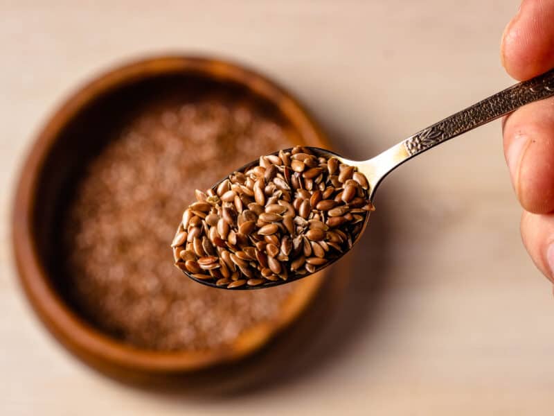 Old-Fashioned Cranberry Bread can be made with flax seeds as an egg replacement - Bowl of flax seeds blurred below a close-up of a spoon full of flaxseeds