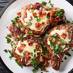 Cooked juicy pork chops with parmesan and bacon closeup on a plate on the table. Horizontal top view from above