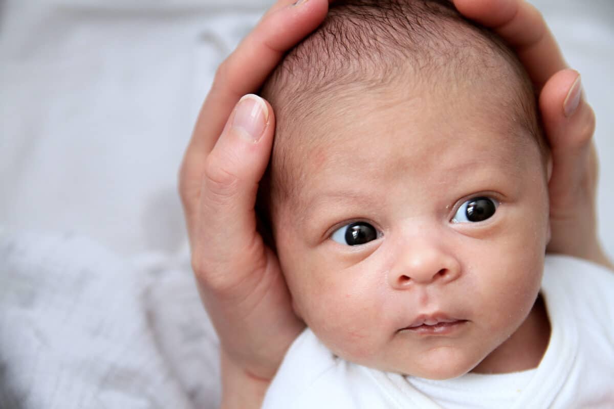 newborn baby with head cradled in adult hands