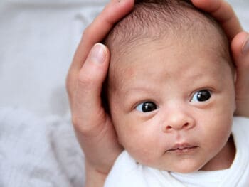 newborn baby with head cradled in adult hands