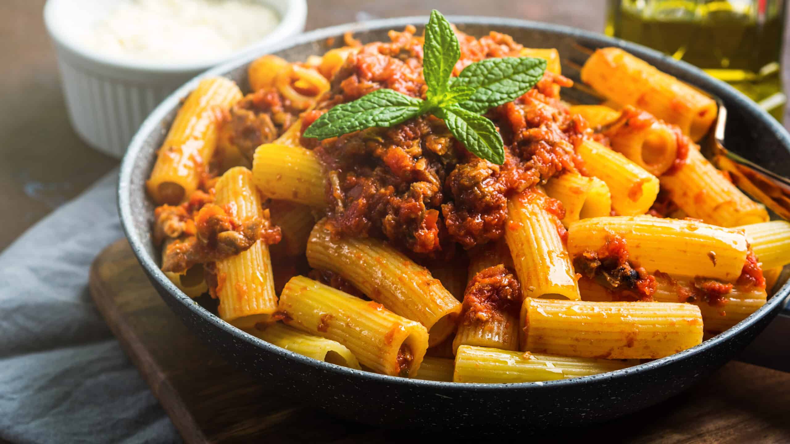 Delicious rigatoni pasta with Italian tomato meat ragu sauce served in a pan on dark brown background. Traditional pasta dish concept. Home made lunch