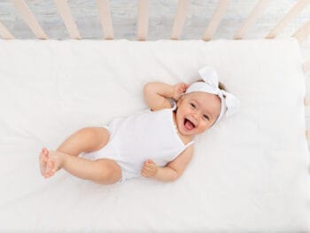 smiling baby in crib laying on her back