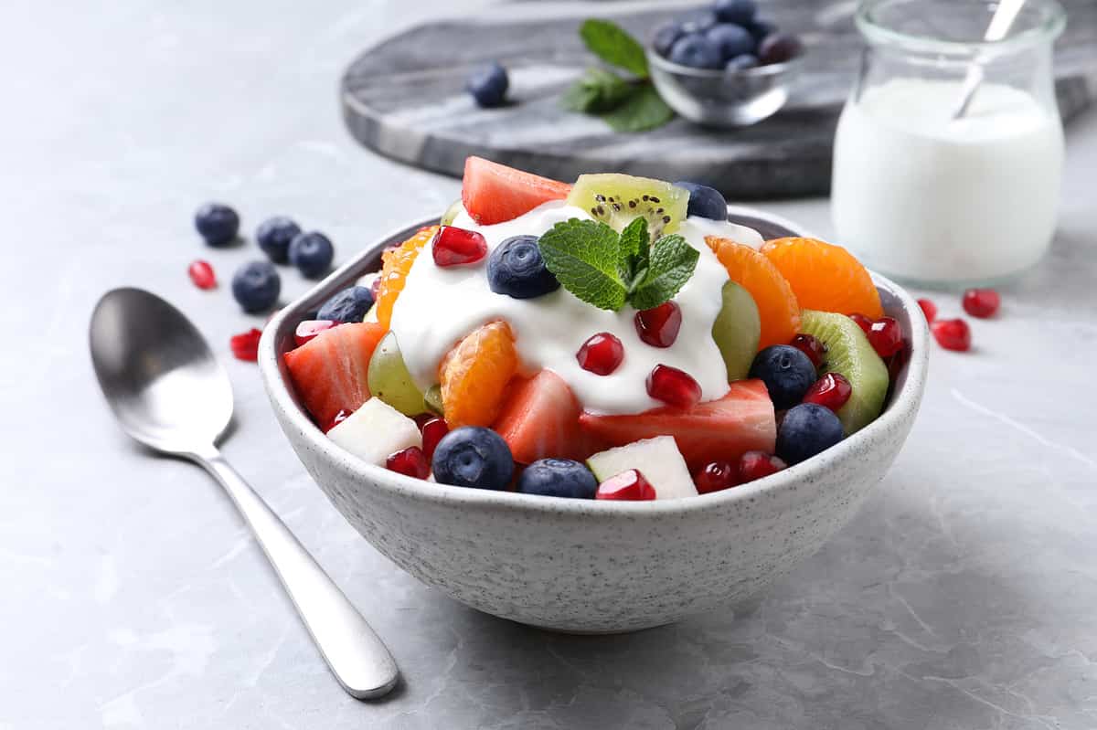 Delicious fruit salad with yogurt on grey table