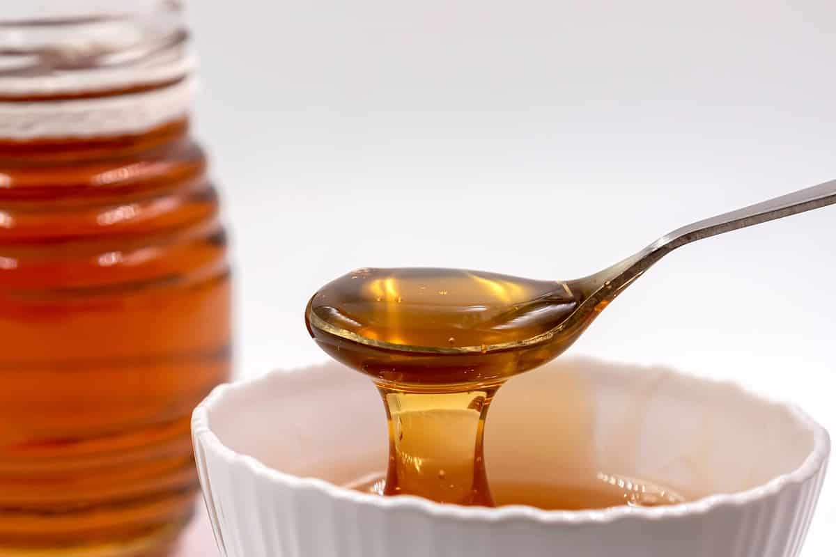 Fresh pure honey in a glass bowl with a honey dripper on the wooden tray.