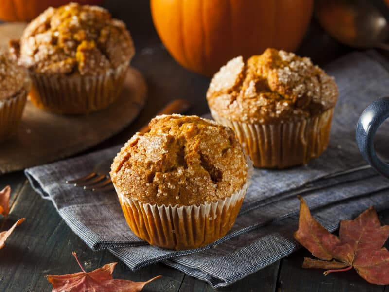Pumpkin molasses muffins give a different spin to a traditional pumpkin recipe. Photo of three muffins surrounded by autumn leaves and a pumpkin.