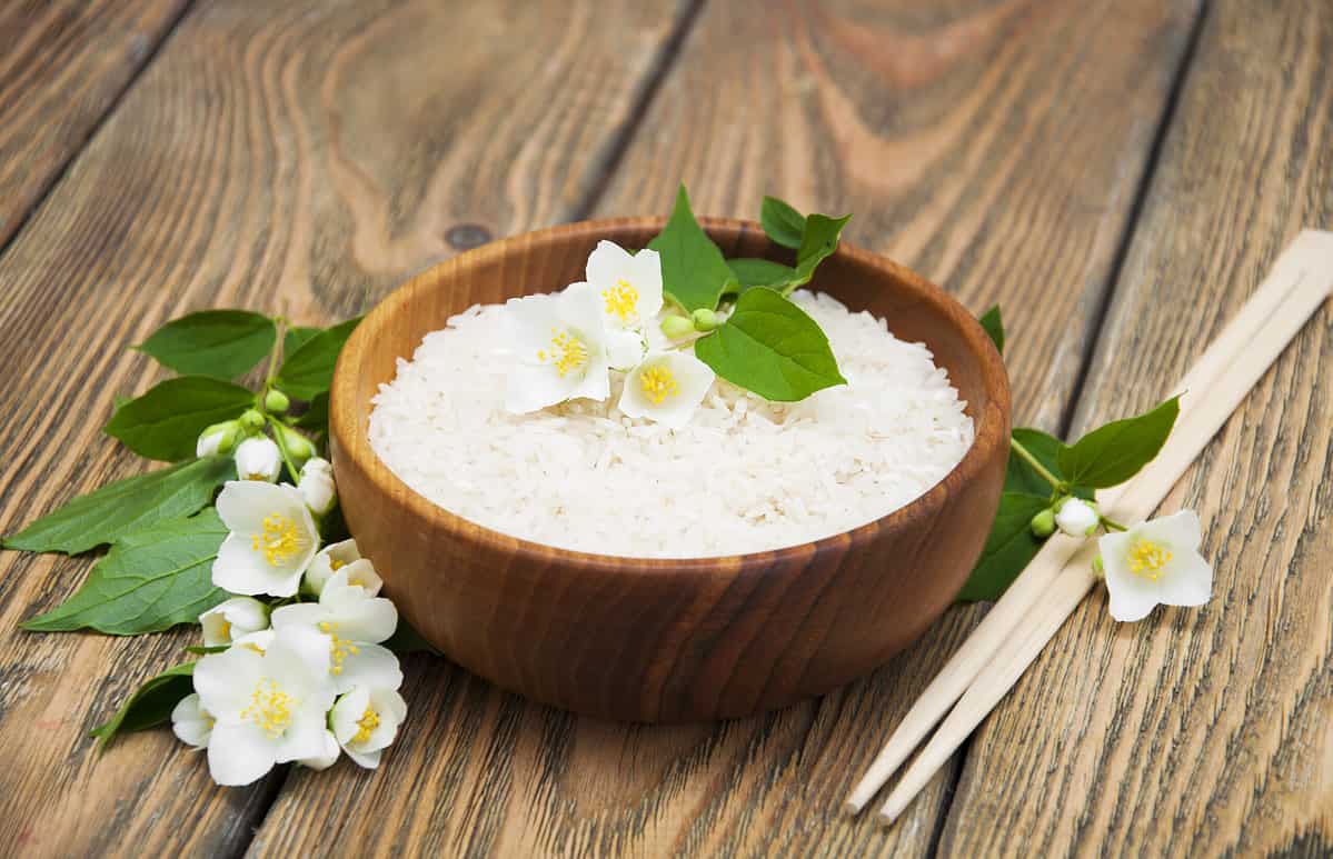 Wooden plate with jasmine rice and jasmine flowers on a wooden background