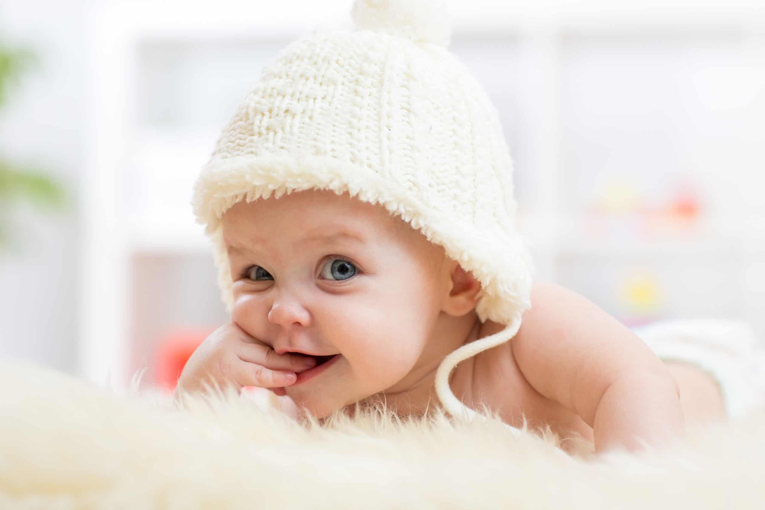 sweet baby laying on her belly on a fluffy rug with knitted cap