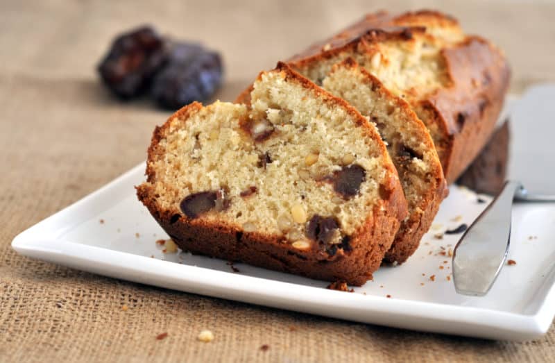 Sliced loaf of date-nut bread on a plate with blurry dates in the background.