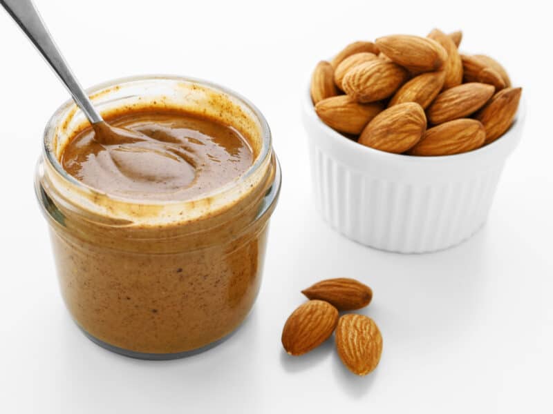 Almond butter (pictured here in a jar next to a cup of raw almonds is the perfect complement to the sweet tanginess in cranberry nut muffins.